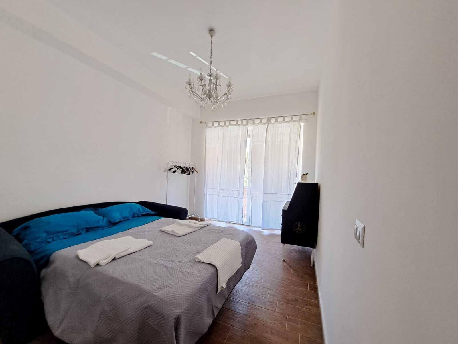 A bedroom with a large bed, a chandelier, a wardrobe, and a window with curtains.