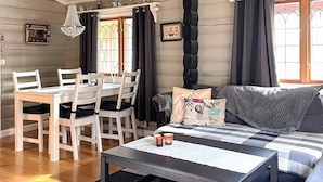 A cozy living room with a wooden dining table, white chairs, a sofa with patterned cushions, and a coffee table. - 4 Star Holiday Home in Fengersfors (Fengersfors)
