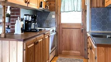 A kitchen with wooden cabinets, a coffee maker, a stove, and a window with a curtain.