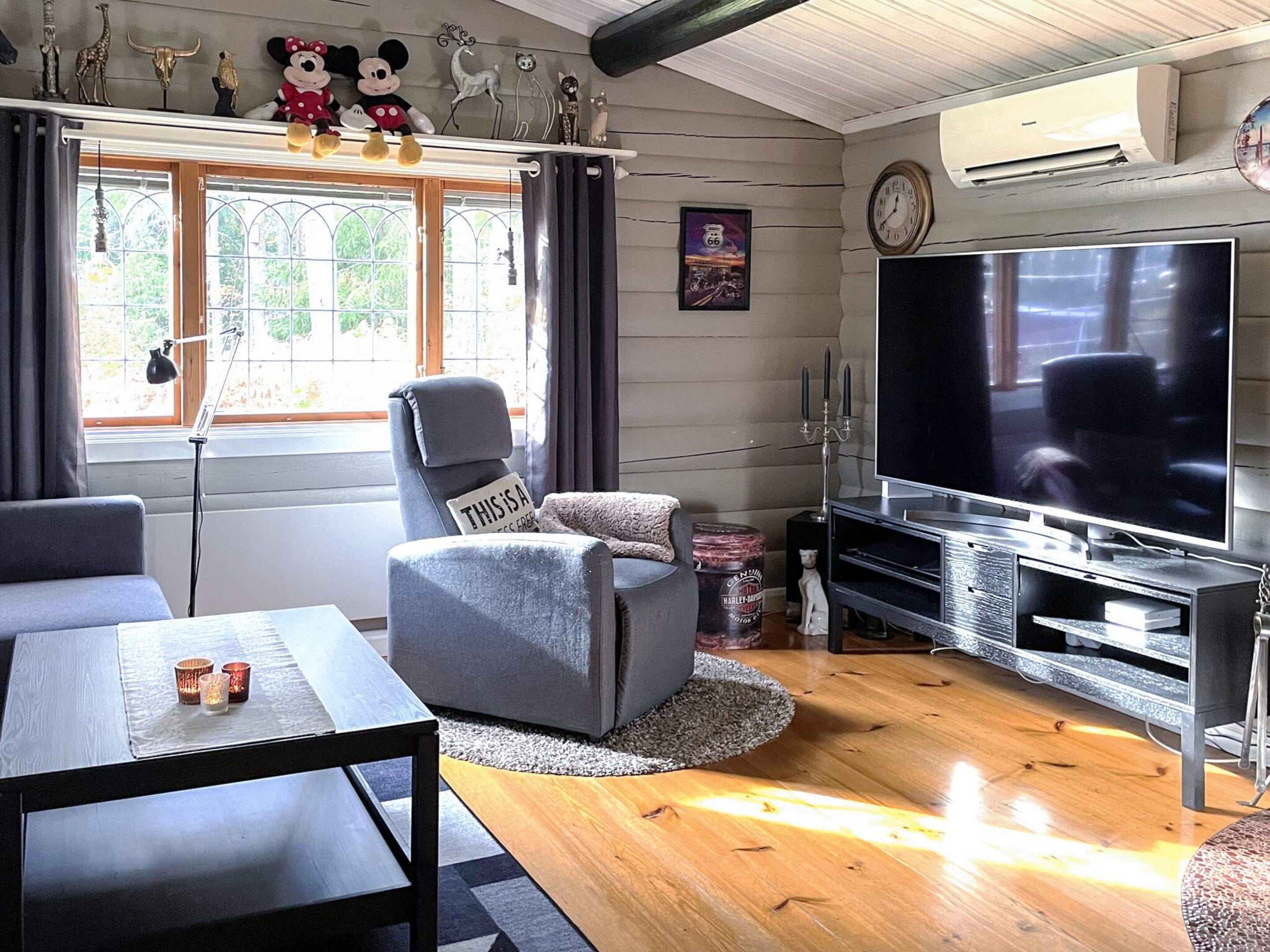 A living room with a television, a grey armchair, a sofa, a coffee table, and a window with curtains.