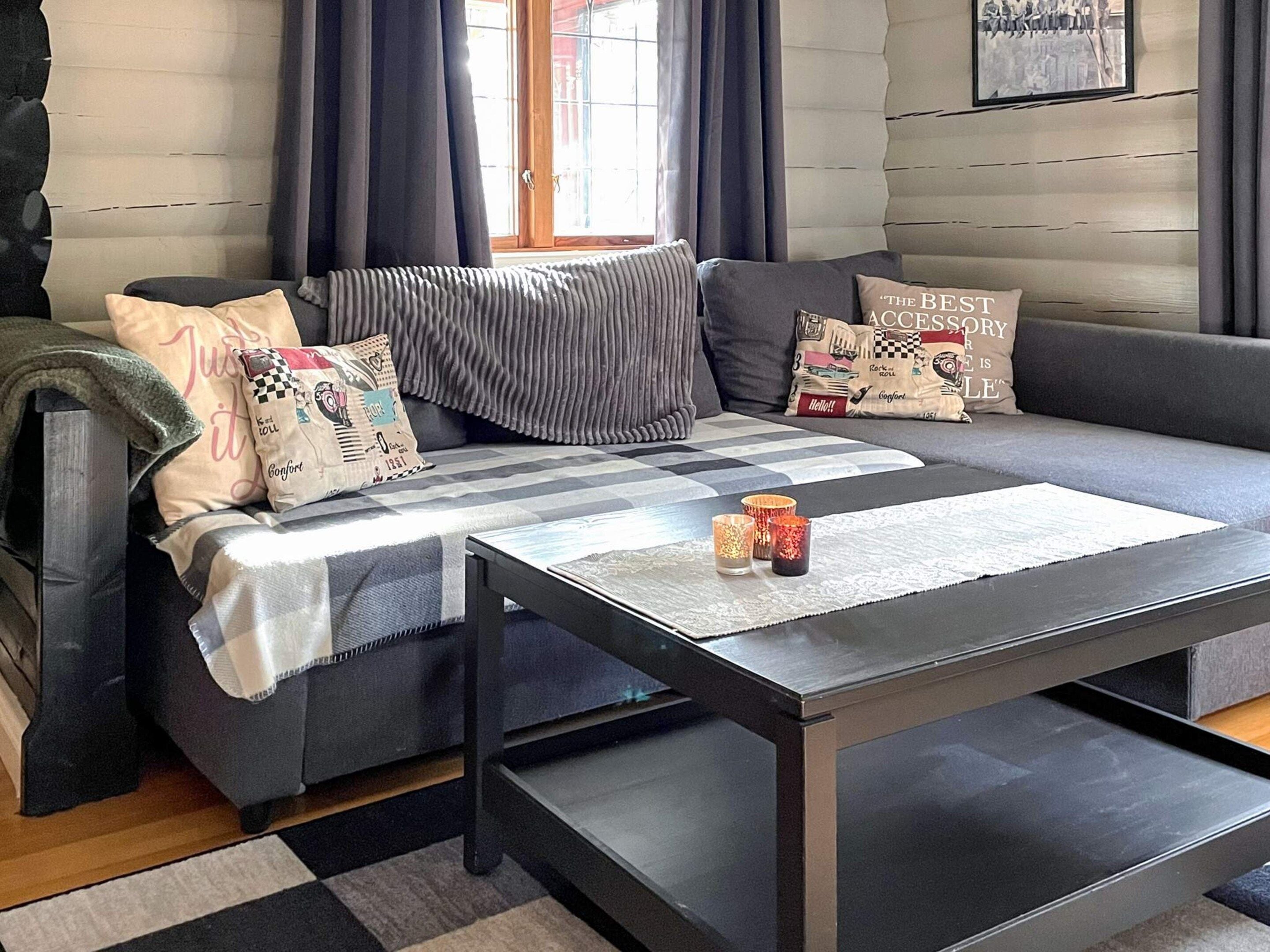 A modern living room with a grey sofa, patterned cushions, a coffee table, and a window with curtains.