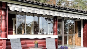 A log cabin with a large window, two chairs, a small table, and a potted plant. - 4 Star Holiday Home in Fengersfors (Fengersfors)