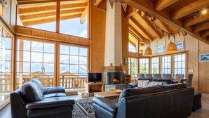 A spacious living room with a fireplace, leather sofas, and large windows offering mountain views. - Chalet in the Heart of Valley With Balcony (Nendaz)