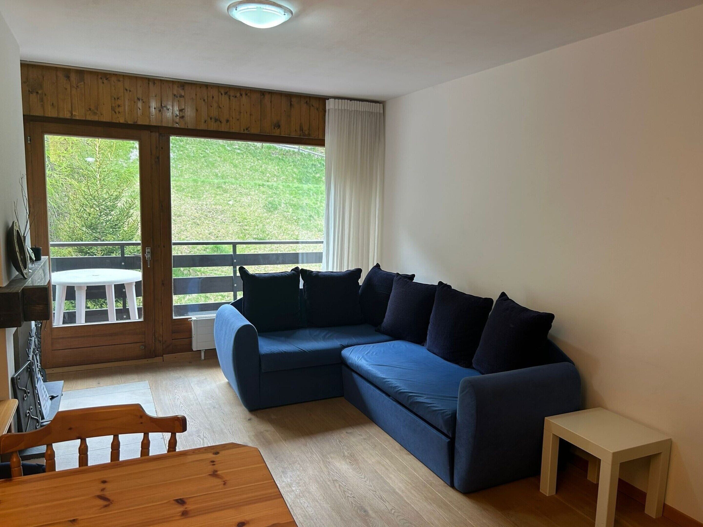 A living room with a blue sectional sofa, a wooden dining table, and a small white side table.