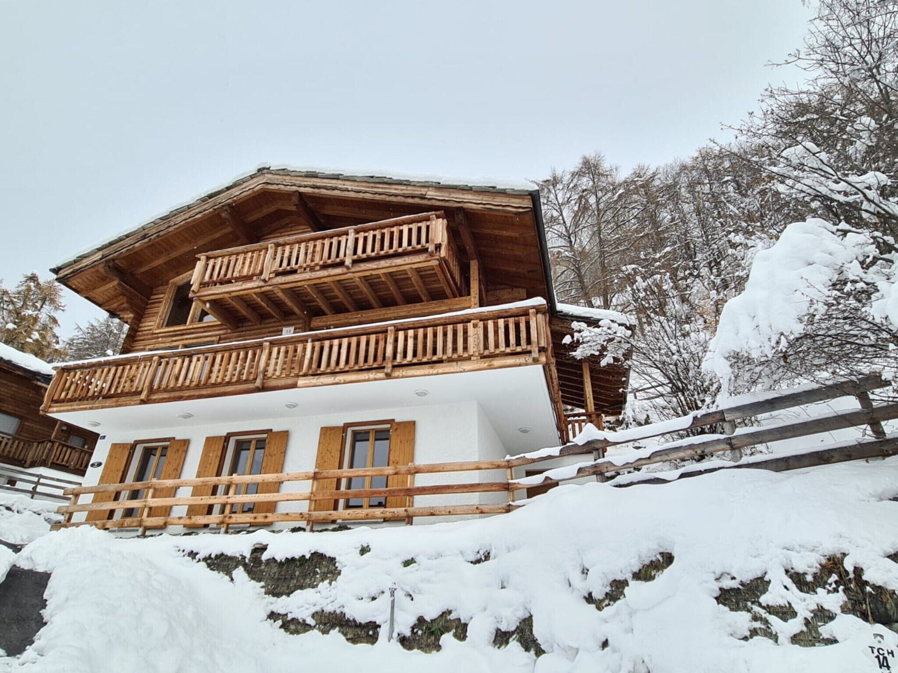 A wooden chalet with a balcony, surrounded by snow-covered trees.