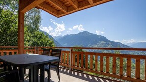Un terrazzo in legno con tavolo e sedie, affacciato su un paesaggio montuoso.