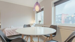 A modern room with a round white table, black chairs, a hanging pendant light, a window with a view of buildings, and a radiator below the window. - 3 Person Holiday Home in Thorshavn (Kjellerup)