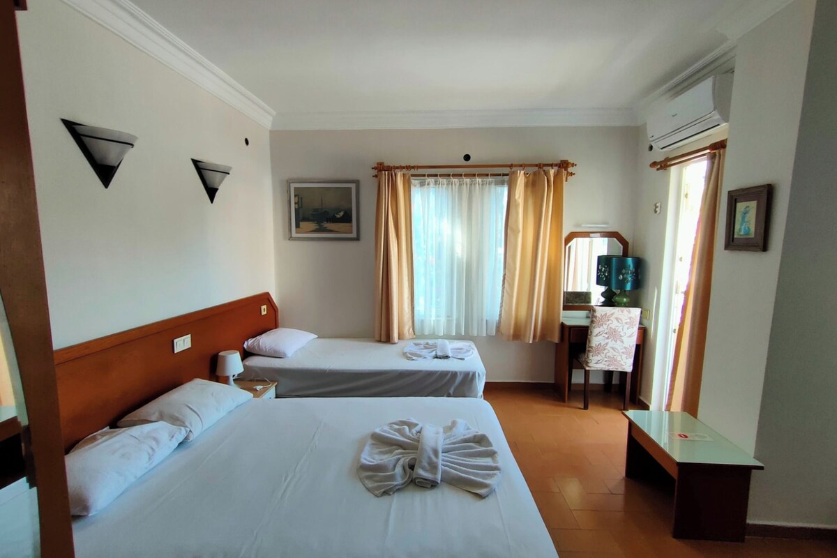 Una habitación de hotel con dos camas, un escritorio, una silla, una lámpara y un cuadro en la pared.