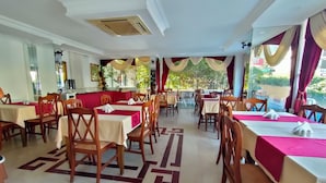 Un restaurante con varias mesas y sillas, piso estampado y grandes ventanales con cortinas.