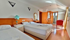 Habitación de hotel con dos camas, una mesita de noche con lámpara, baño visible a través de una puerta abierta y una silla roja.