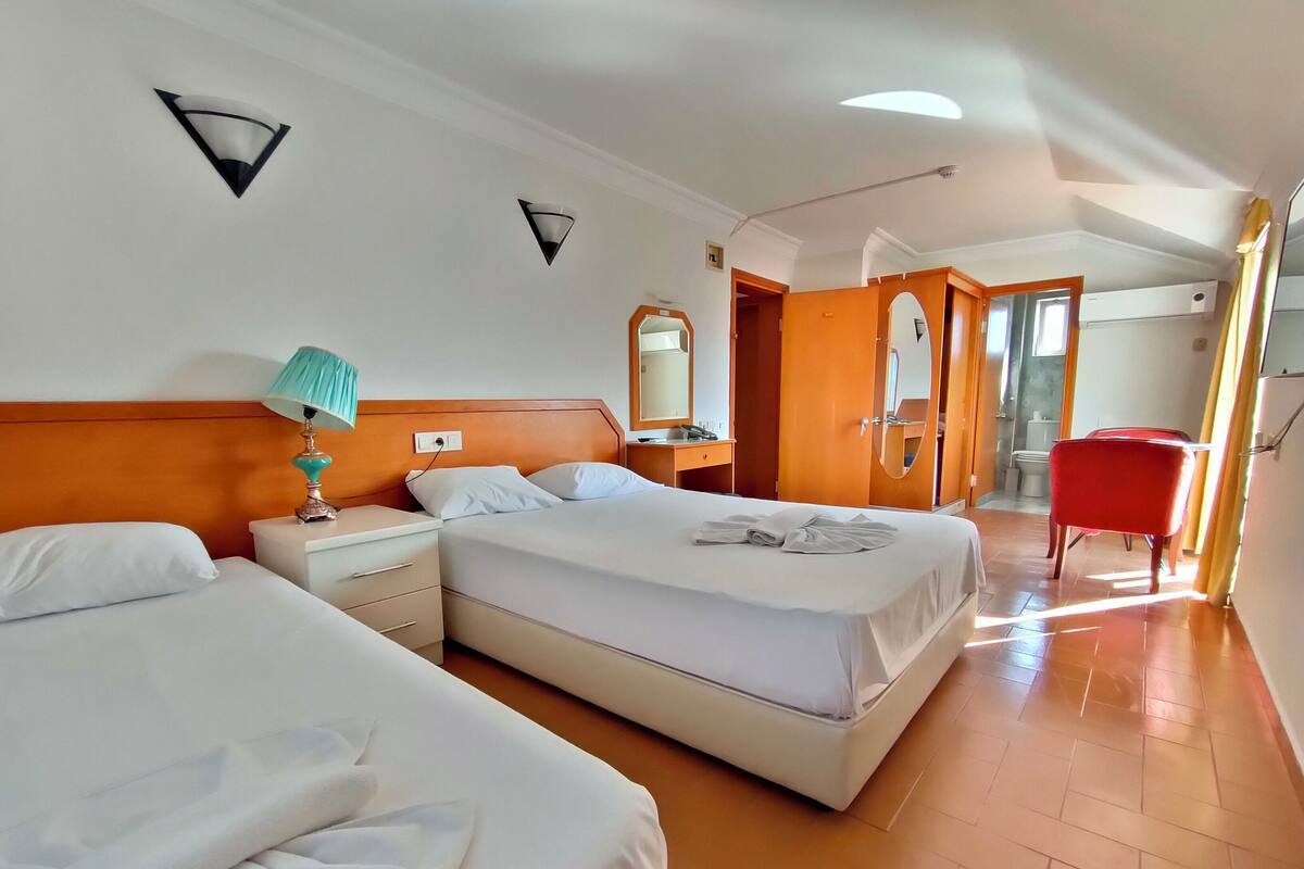 A hotel room with two beds, a nightstand with a lamp, a bathroom visible through an open door, and a red chair.