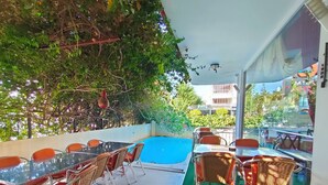 Un espacio al aire libre con mesas, sillas, piscina y vegetación.