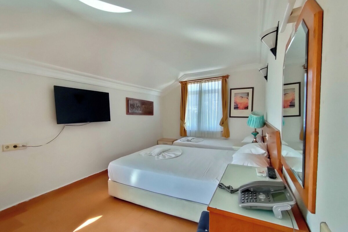 Una camera d'albergo con un letto, una scrivania con il telefono, uno specchio e un televisore appeso al muro.