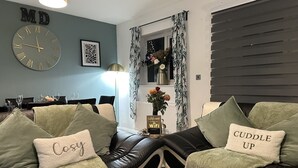 A modern living room with a sofa set, a clock, and a welcome sign. - Bramblemead 5 bed House in Manchester Leigh (Leigh)