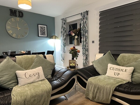 A modern living room with a sofa set, a clock, and a welcome sign.