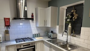 A modern kitchen with white cabinets, a stainless steel range hood, a built-in oven, a sink, and a toaster. - Bramblemead 5 bed House in Manchester Leigh (Leigh)