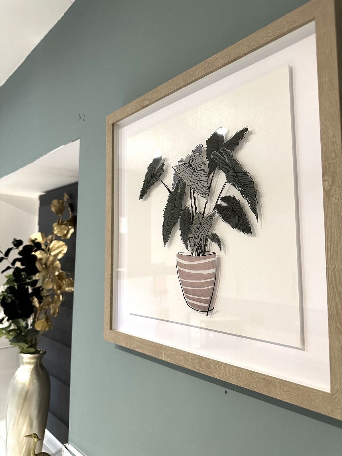 A framed artwork of a plant in a striped pot on a wall.