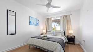 A bedroom with a bed, a ceiling fan, a window with curtains, a nightstand, and a wall-mounted mirror. - New Farm Nest! 2Bed/1Bath/2Car/Balcony (New Farm)
