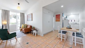 A modern living room with a sofa, a dining table with chairs, a ceiling fan, and a kitchen area with cabinets. - New Farm Nest! 2Bed/1Bath/2Car/Balcony (New Farm)