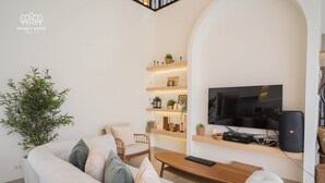 Een moderne woonkamer met een witte bank, een houten salontafel, een aan de muur bevestigde televisie en een boekenkast met decoratieve objecten.