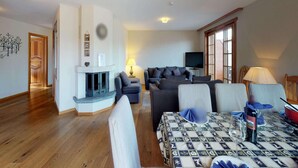 A living room with a fireplace, sofas, a television, and a dining table with a patterned tablecloth. - Comfortable Apartment With Sauna (Veysonnaz)