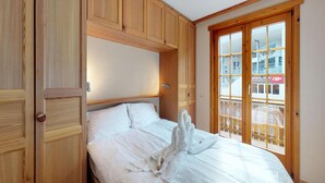 A bedroom with a wooden wardrobe, a bed with white linens, and a sliding glass door to a balcony. - Comfortable Apartment With Sauna (Veysonnaz)