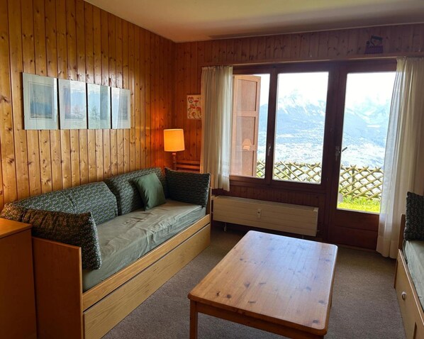 Ein Zimmer in einer Holzhütte mit einer Couch, einem Tisch und einem Fenster mit Bergblick.