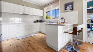 Een moderne keuken met witte kasten, een centraal eiland met barkrukken, een raam met uitzicht en wanddecoratie met een koffie thema.