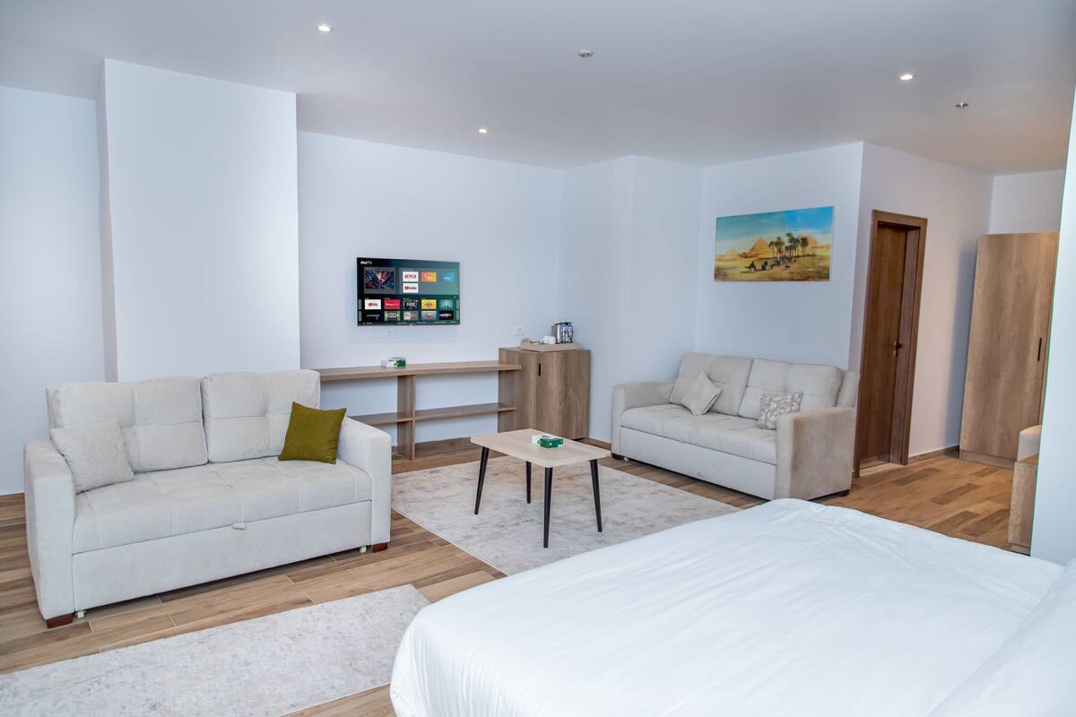 Une chambre d’hôtel moderne et minimaliste, comprenant un lit, deux canapés, une petite table et un téléviseur fixé au mur.