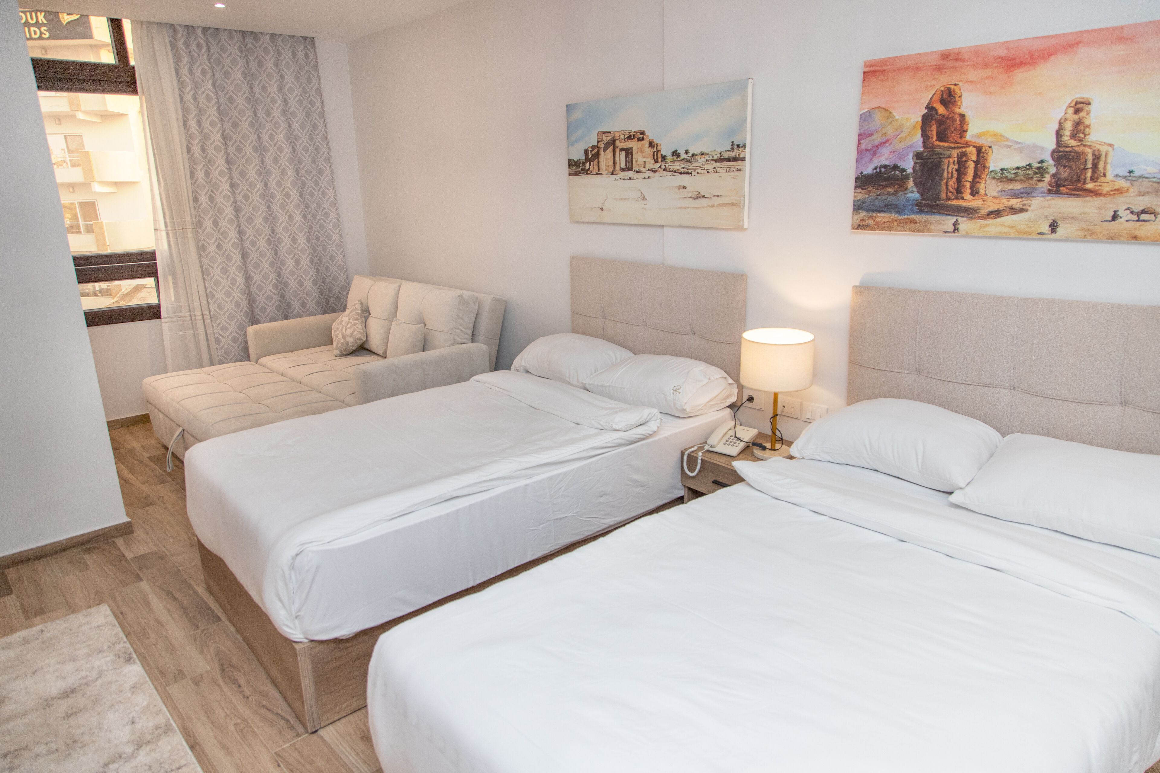 A hotel room with two beds, a sofa, a lamp, and artwork on the walls.