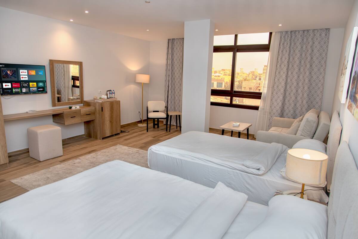 Une chambre d’hôtel avec deux lits, un bureau, une chaise, une télévision et une fenêtre donnant sur la ville.