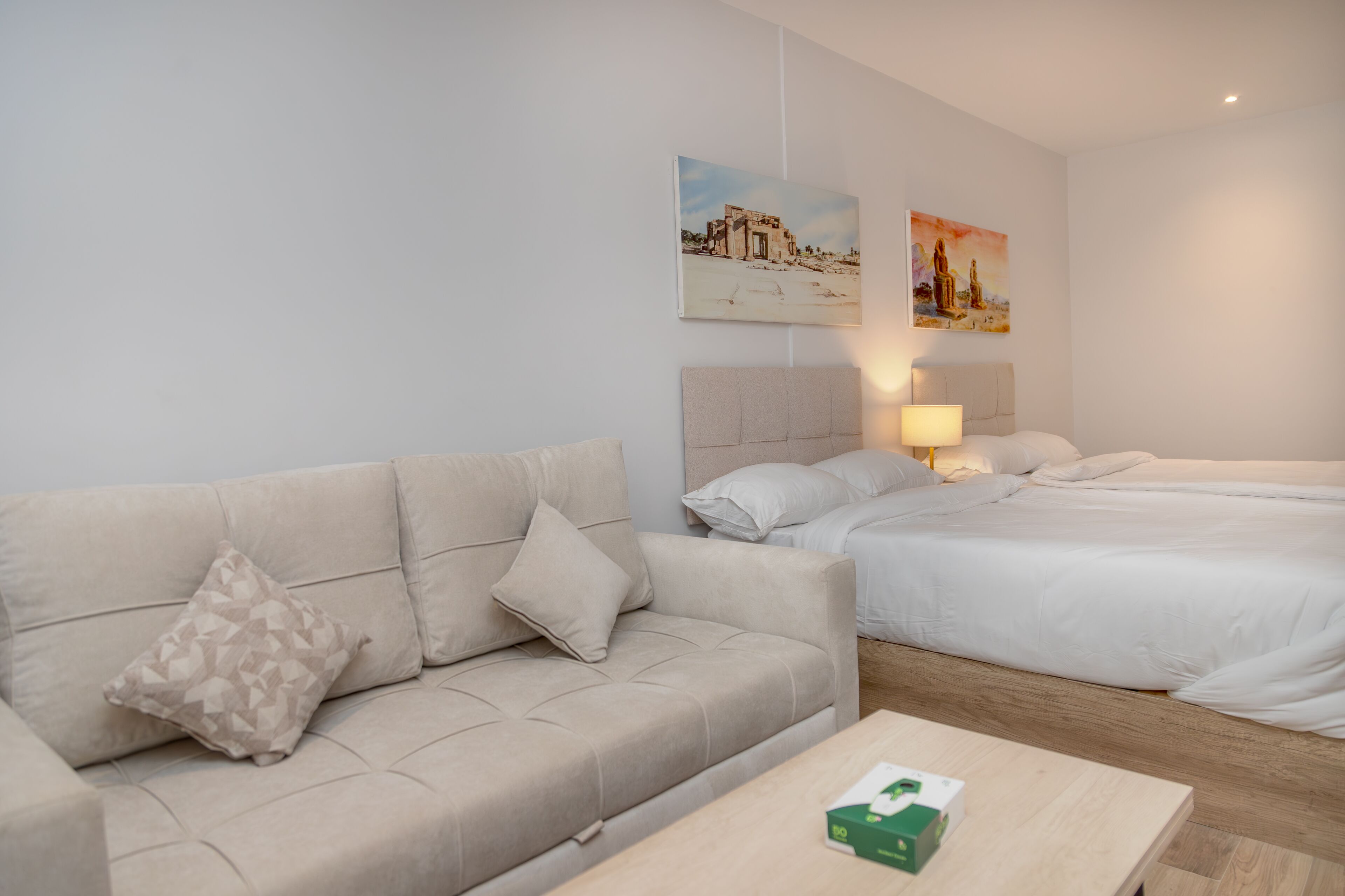 A hotel room with a beige sofa, a single bed, and a wooden coffee table.