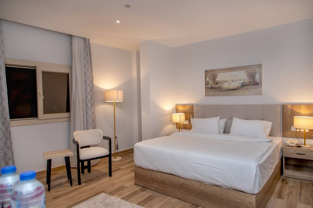 Une chambre d’hôtel avec un grand lit, des lampes de chevet, une chaise, une petite table et un tableau au mur.