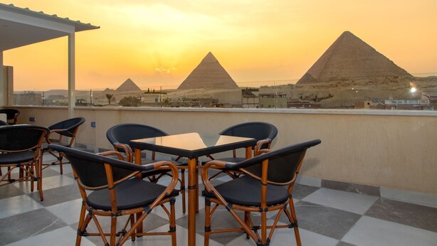 A terrace with wicker chairs and a table, overlooking the pyramids during sunset. - AL Farida Boutique Pyramids (Giza)