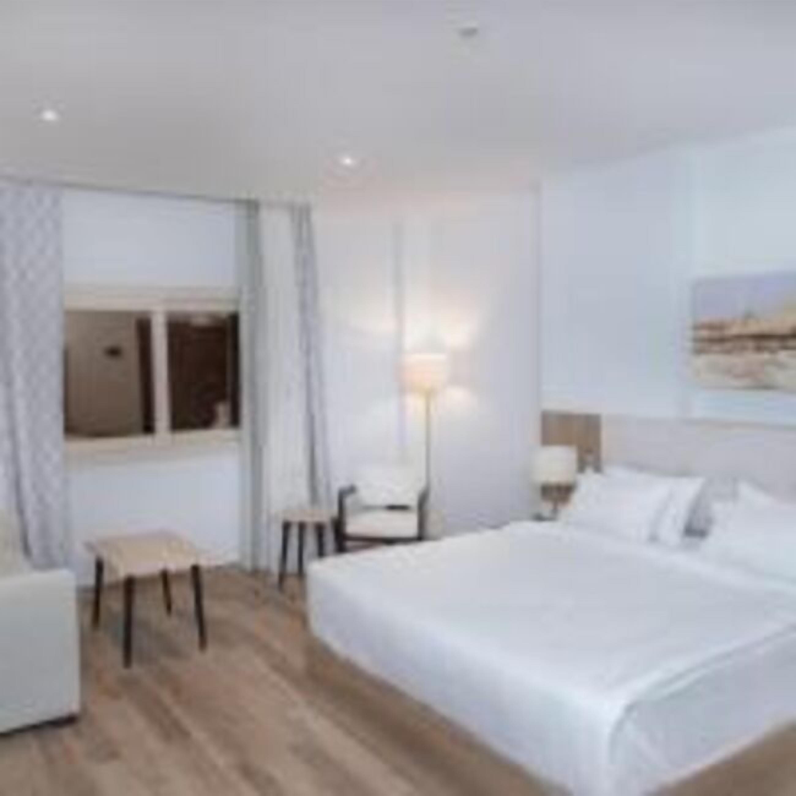 Une chambre d’hôtel avec un grand lit, une petite table, une chaise et une fenêtre.