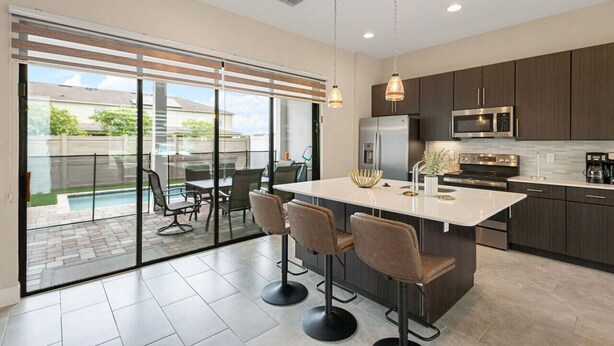 A modern kitchen with a central island, dark cabinetry, stainless steel appliances, and a glass door leading to an outdoor patio area. - Dolce Far Niente - Villa Domani (Davenport)