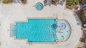 A rectangular swimming pool with a circular hot tub and a water feature in the center, surrounded by a paved deck with lounge chairs and palm trees. - Dolce Far Niente - Villa Domani (Davenport)