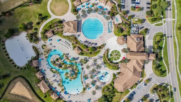 An aerial view of a resort with multiple swimming pools, a large central pool, and a variety of surrounding amenities including parking areas and landscaped gardens.
