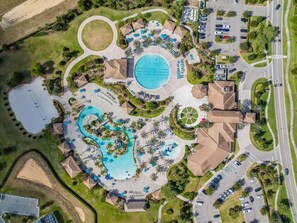 An aerial view of a resort with multiple swimming pools, a large central pool, and a variety of surrounding amenities including parking areas and landscaped gardens.