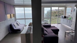A modern living room with a sofa set, a small table, and a kitchen area with cabinets and appliances. - Cliff House (Lombo do Doutor)