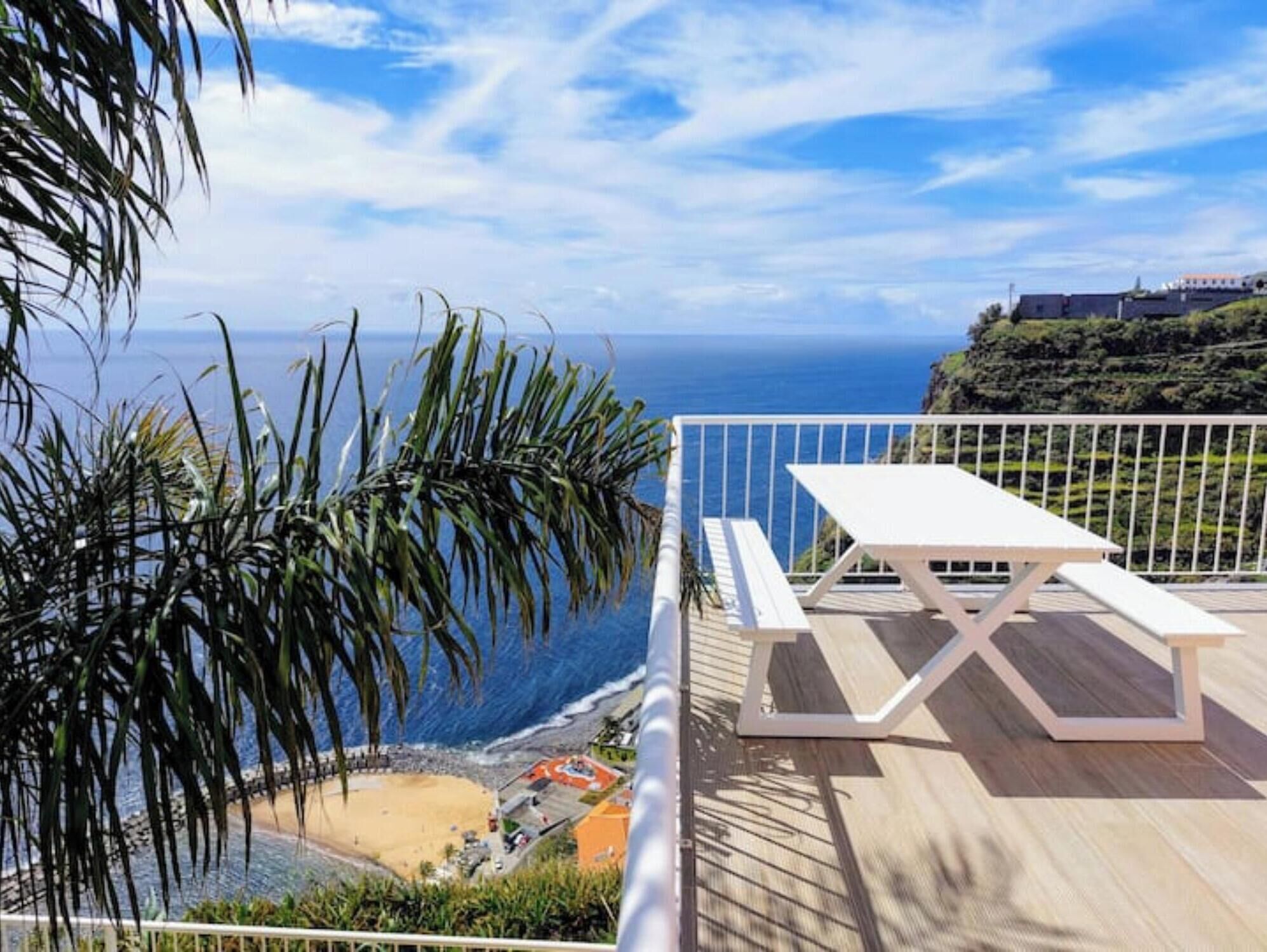 A wooden deck with a white picnic table overlooking a beach and ocean.