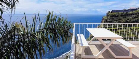 A wooden deck with a white picnic table overlooking a beach and ocean.