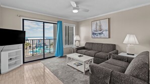 A living room with a sofa, coffee table, TV, and a view of a pool and ocean through a sliding door. - A311 at the Myrtle Beach Resort (Myrtle Beach)
