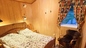 A cozy room with a bed, a chair, a window with curtains, and a lamp. - 7 Person Holiday Home in Lyngdal (Lyngdal)