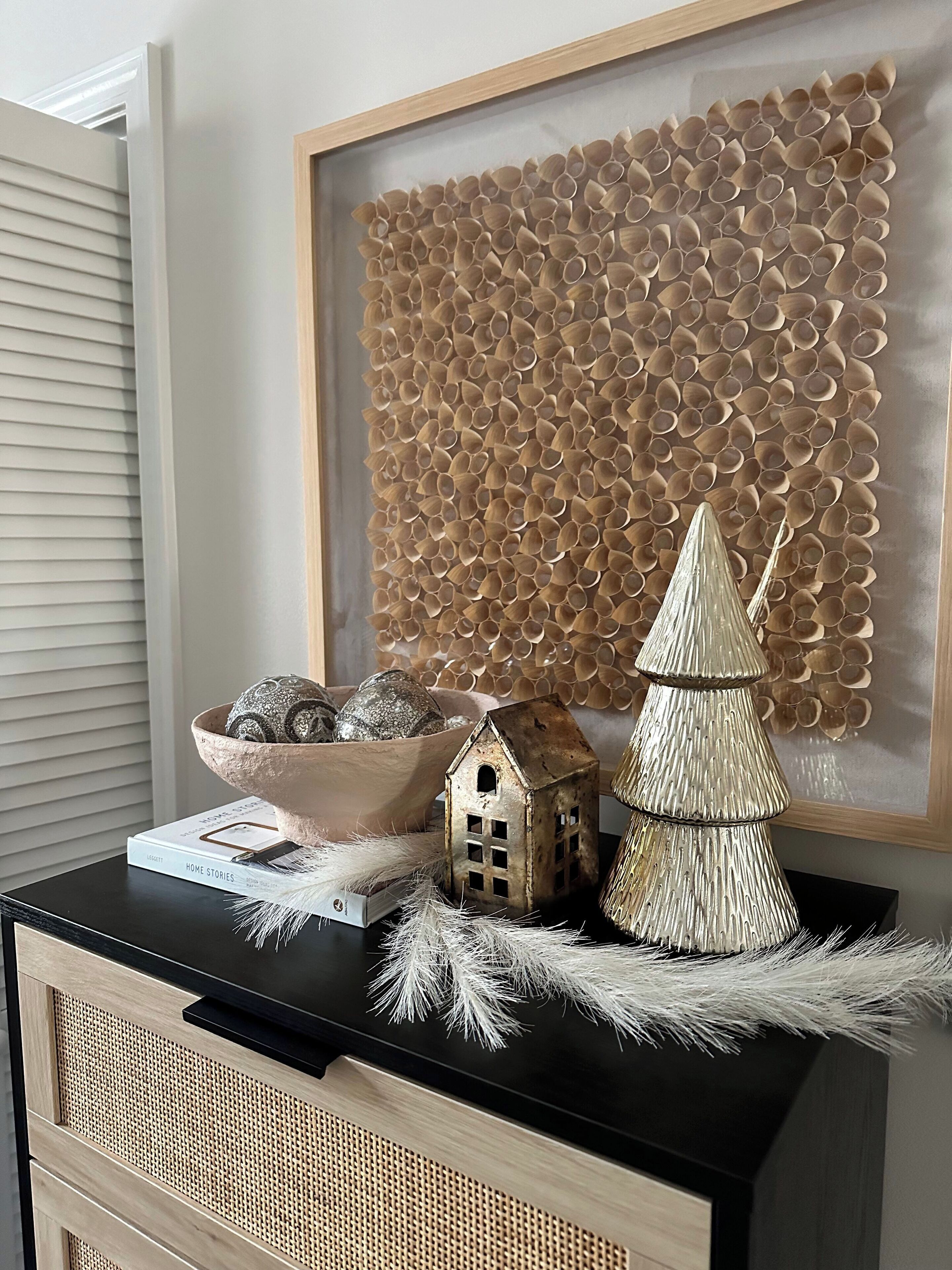 A decorative wall with a textured pattern, a small house model, a Christmas tree, and a bowl of decorative eggs on a black table.