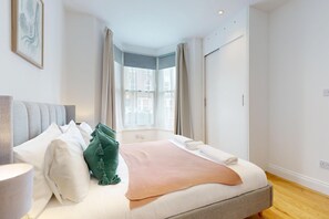 A bedroom with a bed, pillows, a blanket, a bedside table, and a window with curtains.
