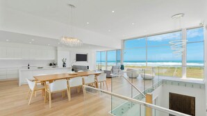 A modern kitchen with a dining area, large windows with a view of the ocean, and a staircase leading to an upper level. - Casa Bianca 50 Esplanade Middleton (Middleton)