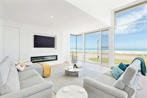 A modern living room with a large TV, comfortable seating, a fireplace, and a view of the beach. - Casa Bianca 50 Esplanade Middleton (Middleton)