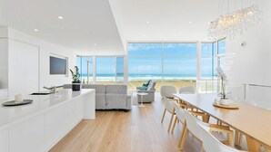 A modern kitchen with a large island, a dining area with a view of the beach, and a living space with a sofa and a plant. - Casa Bianca 50 Esplanade Middleton (Middleton)