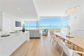 A modern kitchen with a large island, a dining area with a view of the beach, and a living space with a sofa and a plant. - Casa Bianca 50 Esplanade Middleton (Middleton)